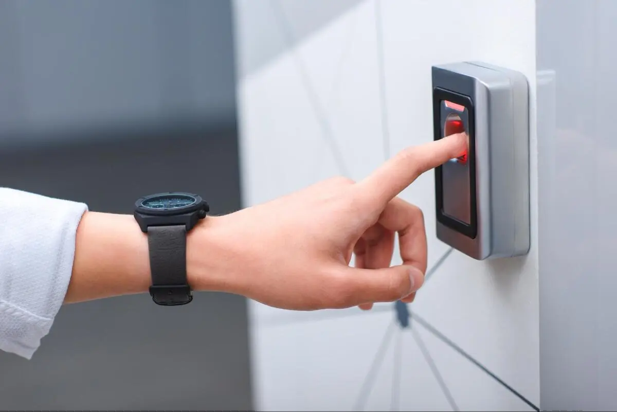 Access control reader at an office entrance Person pressing a finger against a wall-mounted card reader with a red indicator light at an office entrance