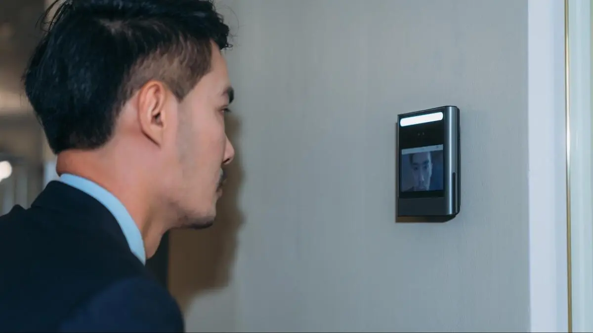 Facial recognition access terminal in an office Man in a suit facing a wall-mounted facial recognition terminal displaying his image on screen